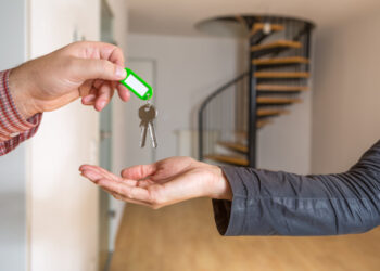 Der Wohnungsschlüssel wird übergeben, im Hintergrund ist eine leere Maisonette Wohnung zu sehen